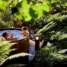 Couple relaxing in a wooden hot tub surrounded by lush native ferns at Secret Spot Rotorua