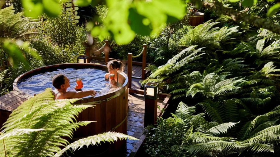 Couple relaxing in a wooden hot tub surrounded by lush native ferns at Secret Spot Rotorua