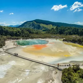 Scenic aerial view of a geothermal pool and boardwalk at Wai-O-Tapu near Rotorua, showcasing vivid orange, yellow, and green mineral colours.