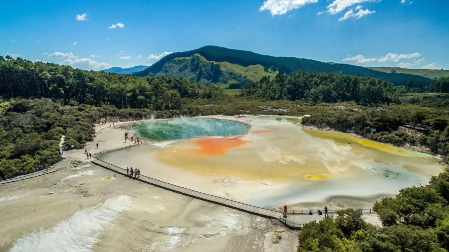 Scenic aerial view of a geothermal pool and boardwalk at Wai-O-Tapu near Rotorua, showcasing vivid orange, yellow, and green mineral colours.