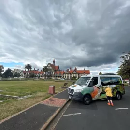 Small group tour van parked near Rotorua Museum and Government Gardens under dramatic skies