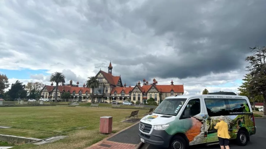 Small group tour van parked near Rotorua Museum and Government Gardens under dramatic skies