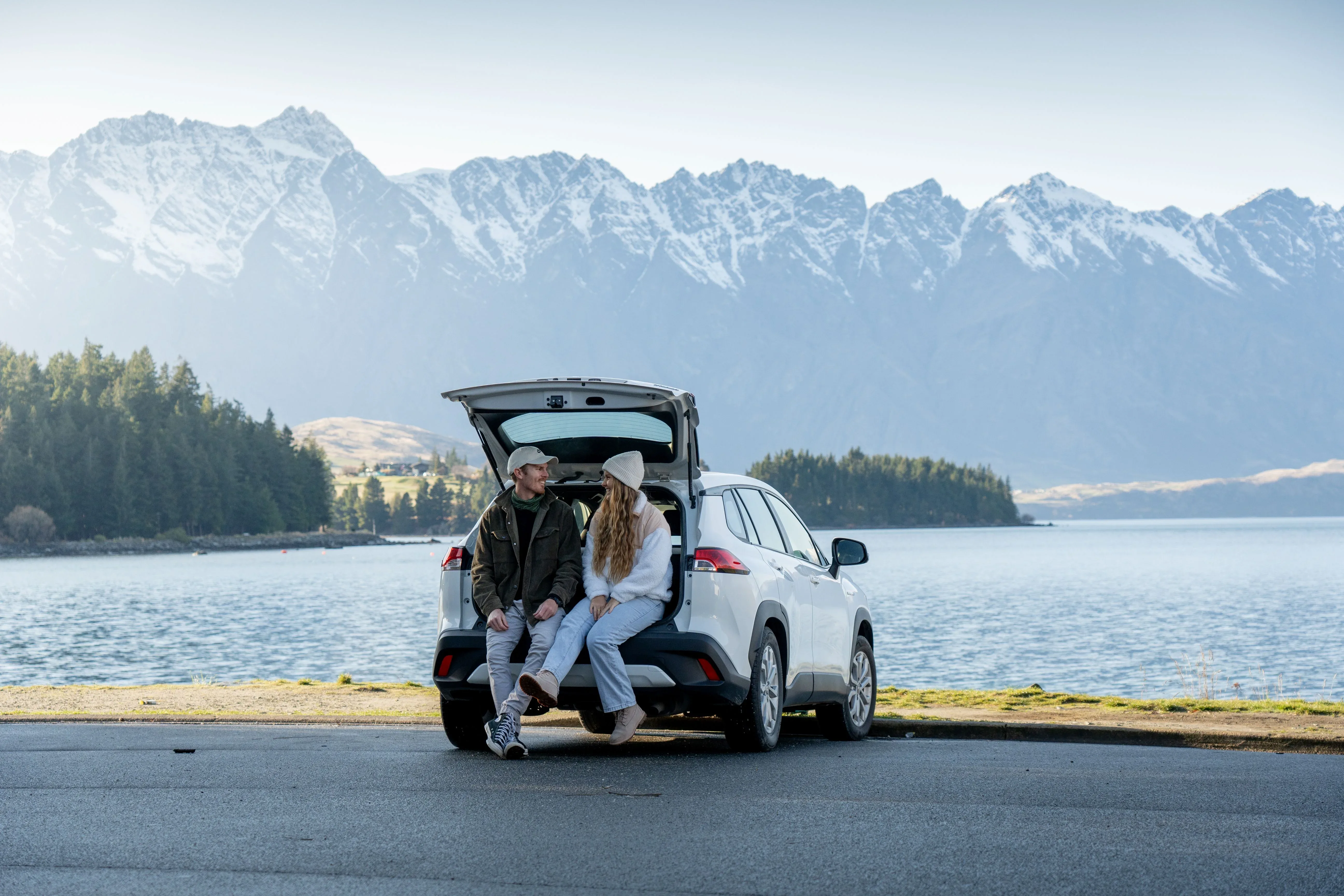 Couple relaxing beside a Toyota RAV4 Hybrid SUV at Lake Wakatipu Queenstown
