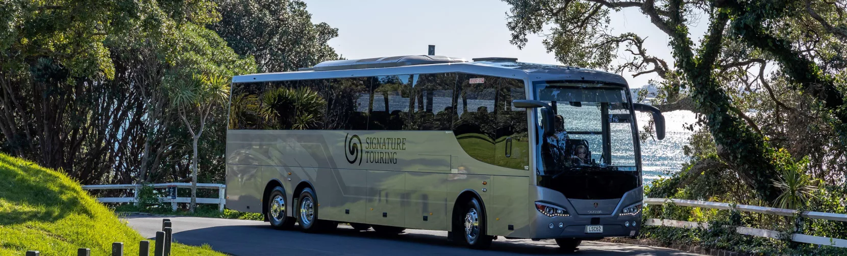 Signature coach from Grand Pacific Tours driving along a scenic coastal road