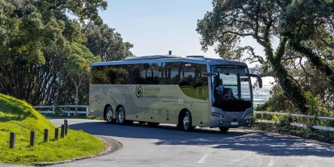 Signature coach from Grand Pacific Tours driving along a scenic coastal road