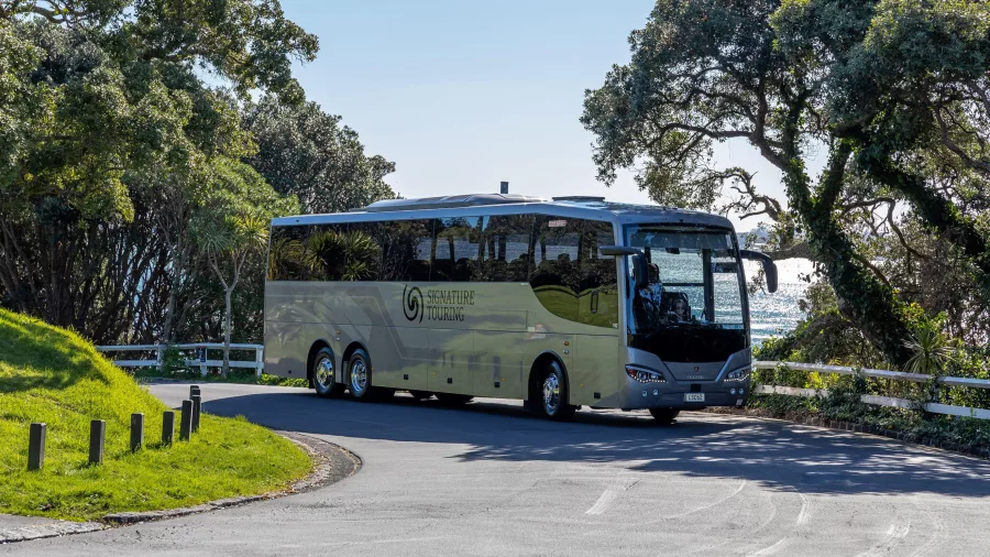 Signature coach from Grand Pacific Tours driving along a scenic coastal road