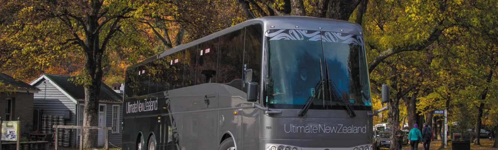 Grand Pacific Ultimate coach parked beneath golden autumn trees in a New Zealand village