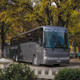 Grand Pacific Ultimate coach parked beneath golden autumn trees in a New Zealand village