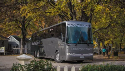 Grand Pacific Ultimate coach parked beneath golden autumn trees in a New Zealand village