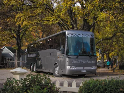 Grand Pacific Ultimate coach parked beneath golden autumn trees in a New Zealand village