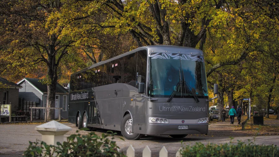 Grand Pacific’s Ultimate coach parked beneath autumn trees in a scenic village