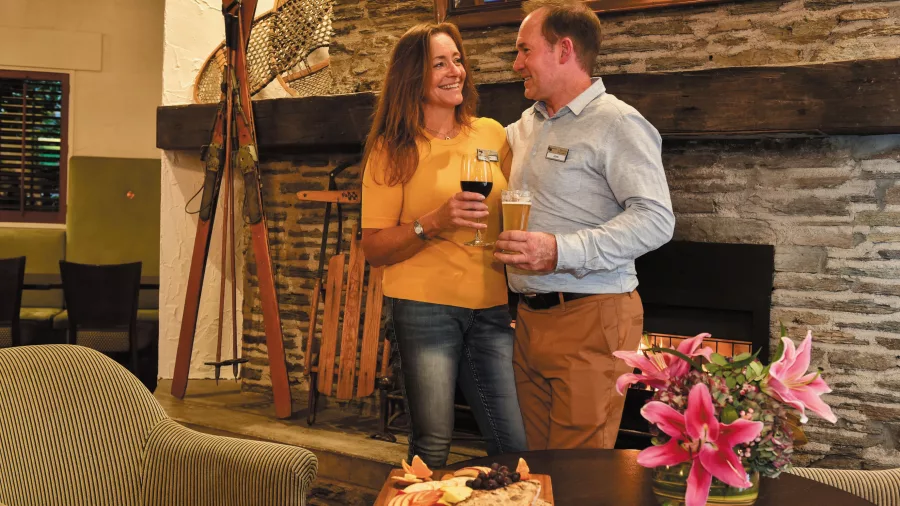 Couple enjoying wine and craft beer by the fireplace during an Ultimate New Zealand coach tour