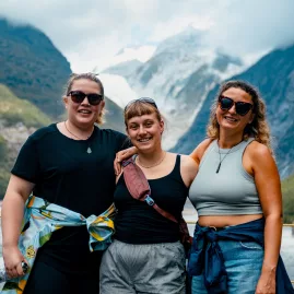 Three travellers posing in front of Franz Josef Glacier on the West Coast of New Zealand