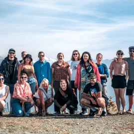 Group of travellers posing by Lake Taupō with mountains in the distance