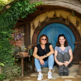 Two women sitting at a blue round door on the Hobbiton Movie Set tour in Matamata, New Zealand