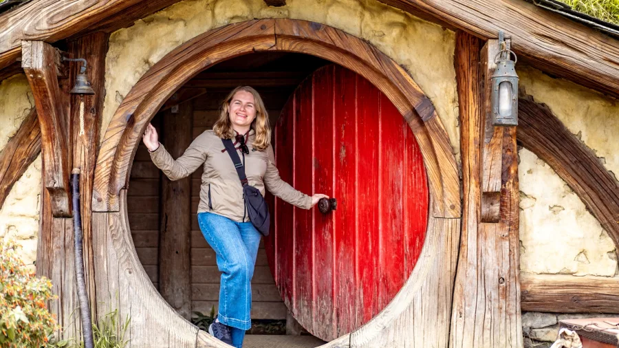 Smiling traveller at iconic red door in Hobbiton Movie Set, Matamata