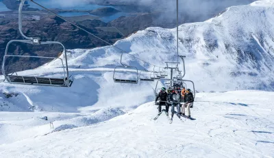 Skiers on chairlift with sweeping alpine views at Treble Cone