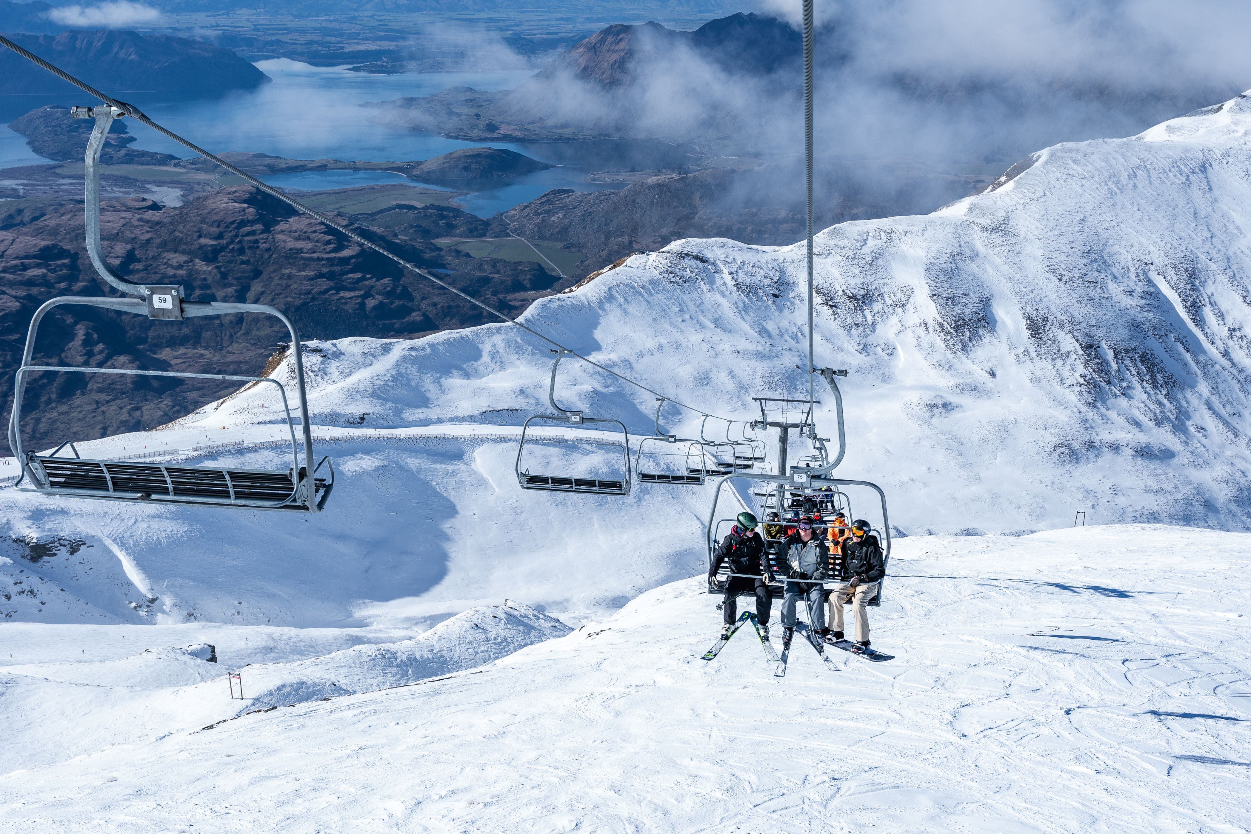 Skiers on chairlift with sweeping alpine views at Treble Cone