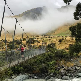 Hiker crossing a swing bridge in Mount Aspiring National Park on a misty day