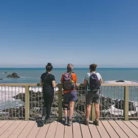 Three hikers standing at the Cape Foulwind lookout deck overlooking the Tasman Sea near Westport