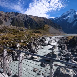 Woman hiking across a swing bridge on the Hooker Valley Track in Aoraki Mount Cook National Park