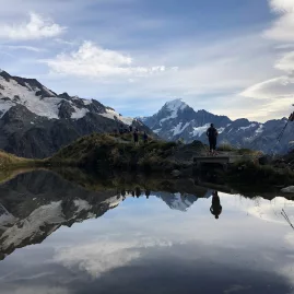 Hikers walking near a reflective tarn on the Red Tarn Track with Mount Cook in the background