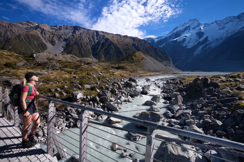 Woman hiking across a swing bridge on the Hooker Valley Track in Aoraki Mount Cook National Park