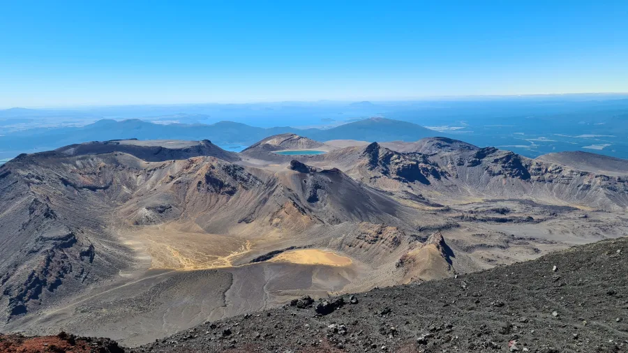 Aerial view of the Tongariro Alpine Crossing with volcanic craters, rugged terrain, and distant views over the North Island of New Zealand.