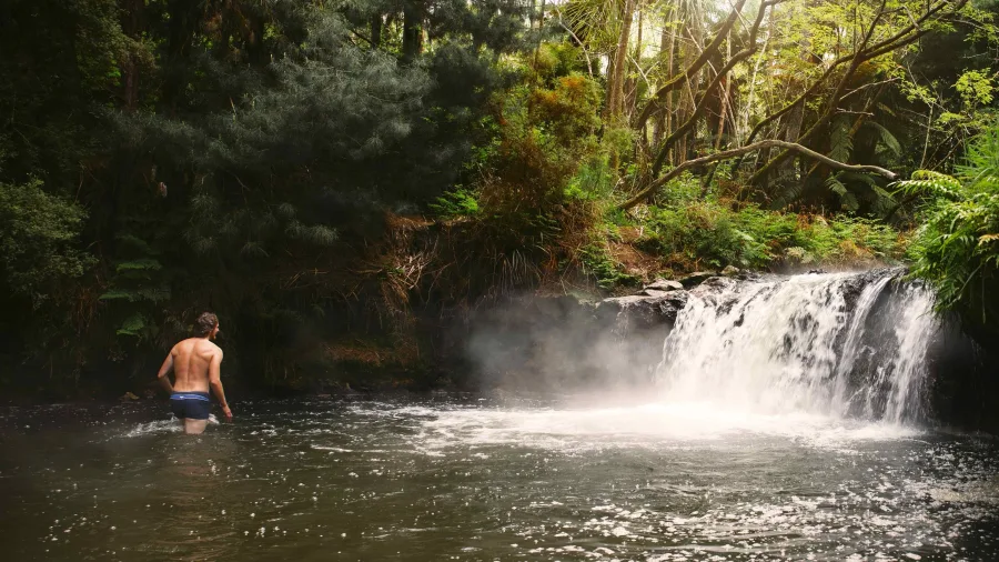 Person standing in the warm waters below the steaming waterfall at Kerosene Creek