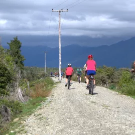 Group of cyclists riding along a gravel section of the West Coast Wilderness Trail with stormy mountains ahead