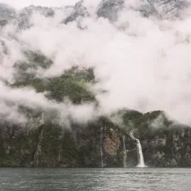 Clouds and mist surround cascading waterfalls in Milford Sound, New Zealand