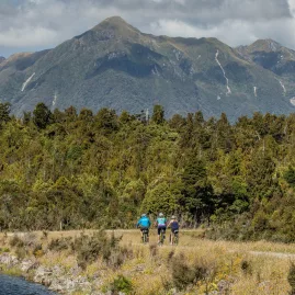 Group of people hiking and biking the West Coast Wilderness Trail with mountains in the background