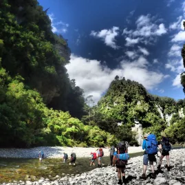 Group of trampers hiking through river valley near Ballroom Overhang, Paparoa National Park