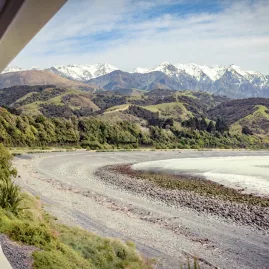 Scenic view from the Coastal Pacific train near Kaikōura with snow-capped mountains and rocky beach