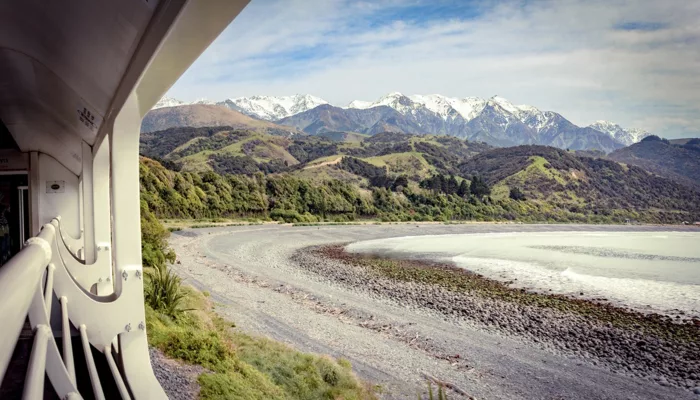 Scenic view from the Coastal Pacific train near Kaikōura with snow-capped mountains and rocky beach