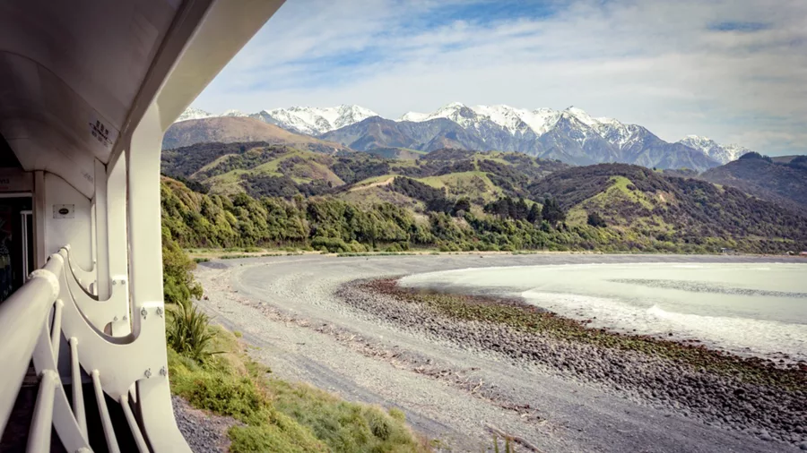 Scenic view from the Coastal Pacific train near Kaikōura with snow-capped mountains and rocky beach