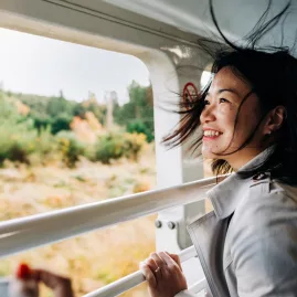 Smiling woman enjoying the view from TranzAlpine viewing carriage
