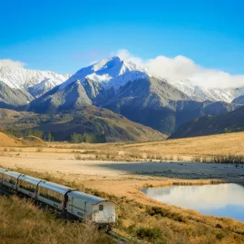 TranzAlpine train beside Lake Sarah with snowy mountain backdrop