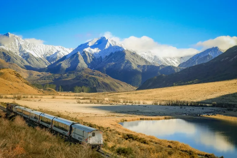 TranzAlpine train beside Lake Sarah with snowy mountain backdrop