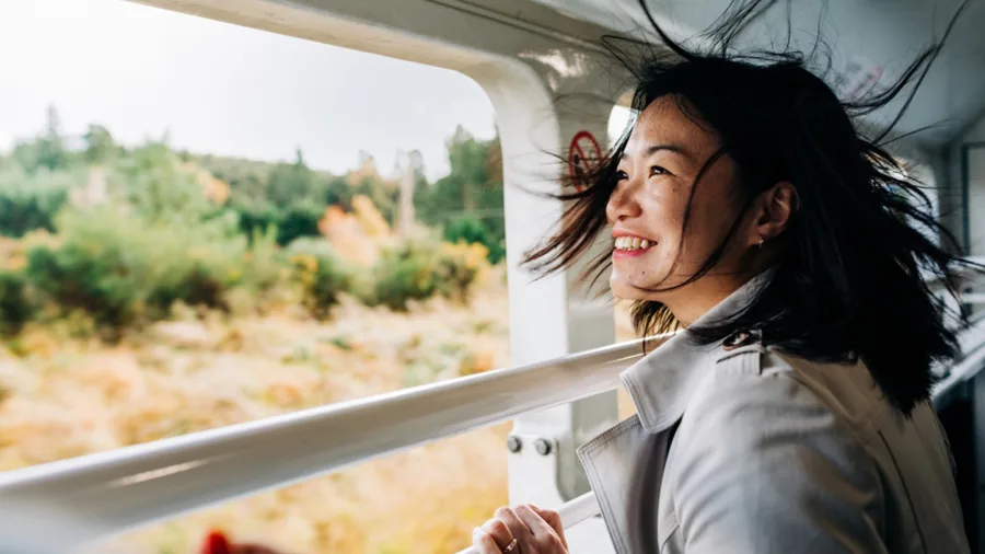 Smiling woman enjoying the view from TranzAlpine viewing carriage