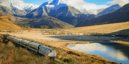 TranzAlpine train beside Lake Sarah with snowy mountain backdrop