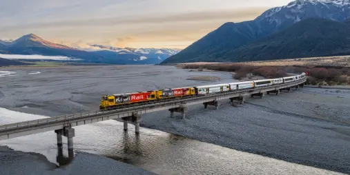 TranzAlpine train crossing Cass River with Southern Alps backdrop