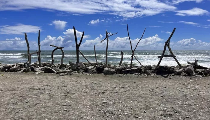Hokitika driftwood sign on the beach with ocean backdrop on New Zealand’s West Coast
