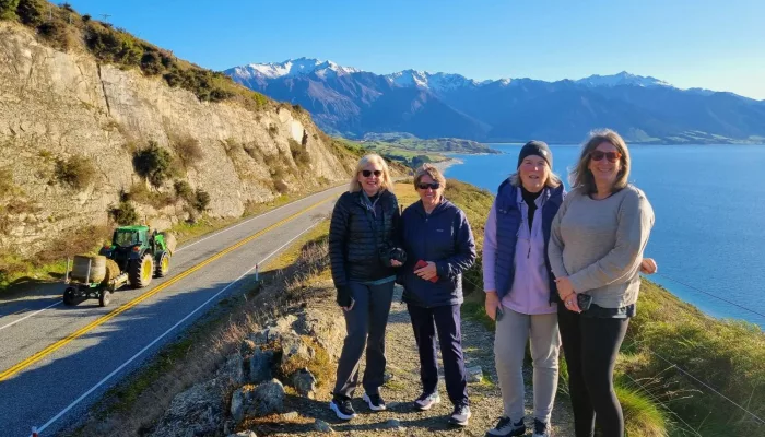 MoaTrek travellers pausing roadside at Lake Hāwea with a passing tractor