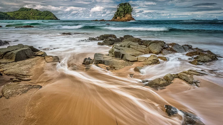 Long exposure of waves flowing over rocks on Coromandel beach at dawn