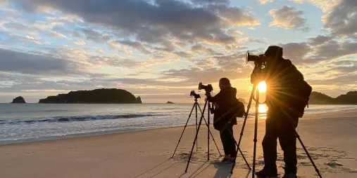 Photographers at sunrise capturing sea stack from Coromandel beach