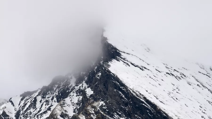 Misty clouds obscure the summit of a snow-covered alpine peak in New Zealand