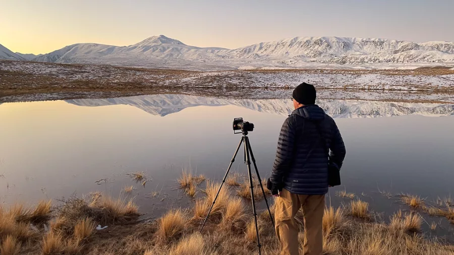 Photographer capturing alpine reflections at a still lake in the Tekapo Basin