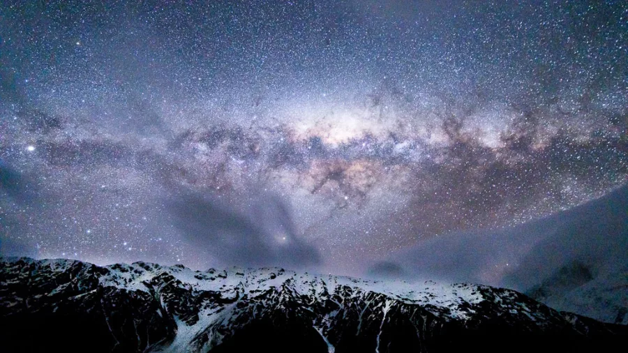 Milky Way arching above snow‑covered mountains under a star-filled sky
