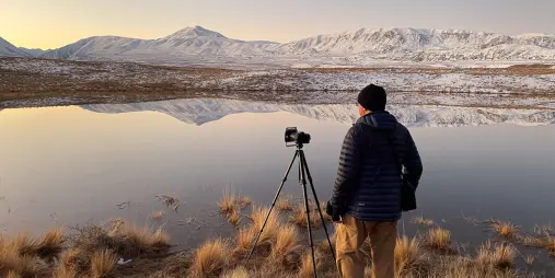 Photographer capturing alpine reflections at a still lake in the Tekapo Basin